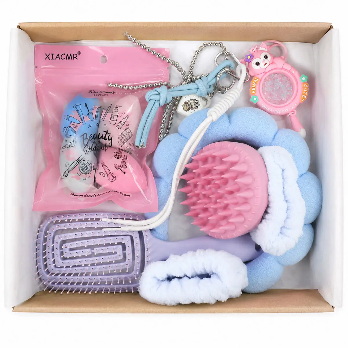 Caja abierta del combo con las siete piezas: esponjas, cepillo lila, masajeador rosa, vincha celeste, muñequeras y dos charms