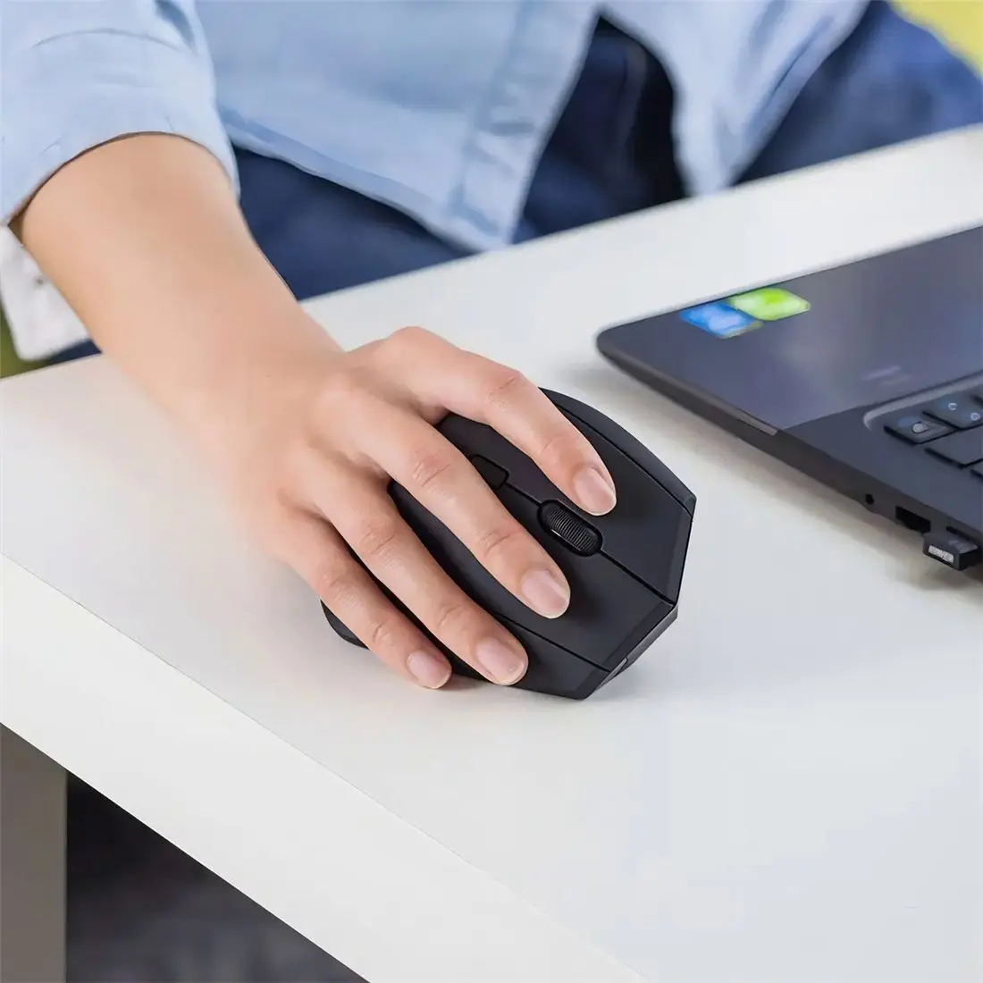 Una persona usando el mouse vertical frente a una notebook